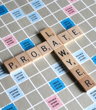 Wooden letter tiles spell out the words 'PROBATE' and 'LAWYER' on a Scrabble board. The board features a grid with colored squares marked with different point values such as 'Double Word Score' and 'Triple Letter Score'.